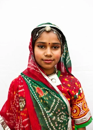 Portrait of a young girl in traditional Rajasthani clothing with patterned red and green fabrics, intricate silver jewelry, and a serene expression.