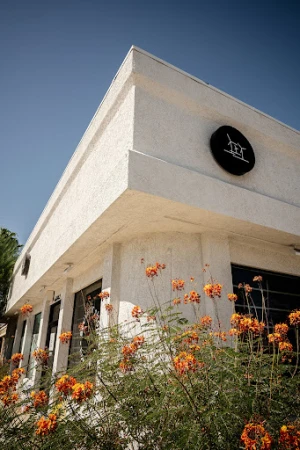 Exterior shot of a modern white building with a round black sign, complemented by vibrant orange flowers in the foreground under a clear sky.
