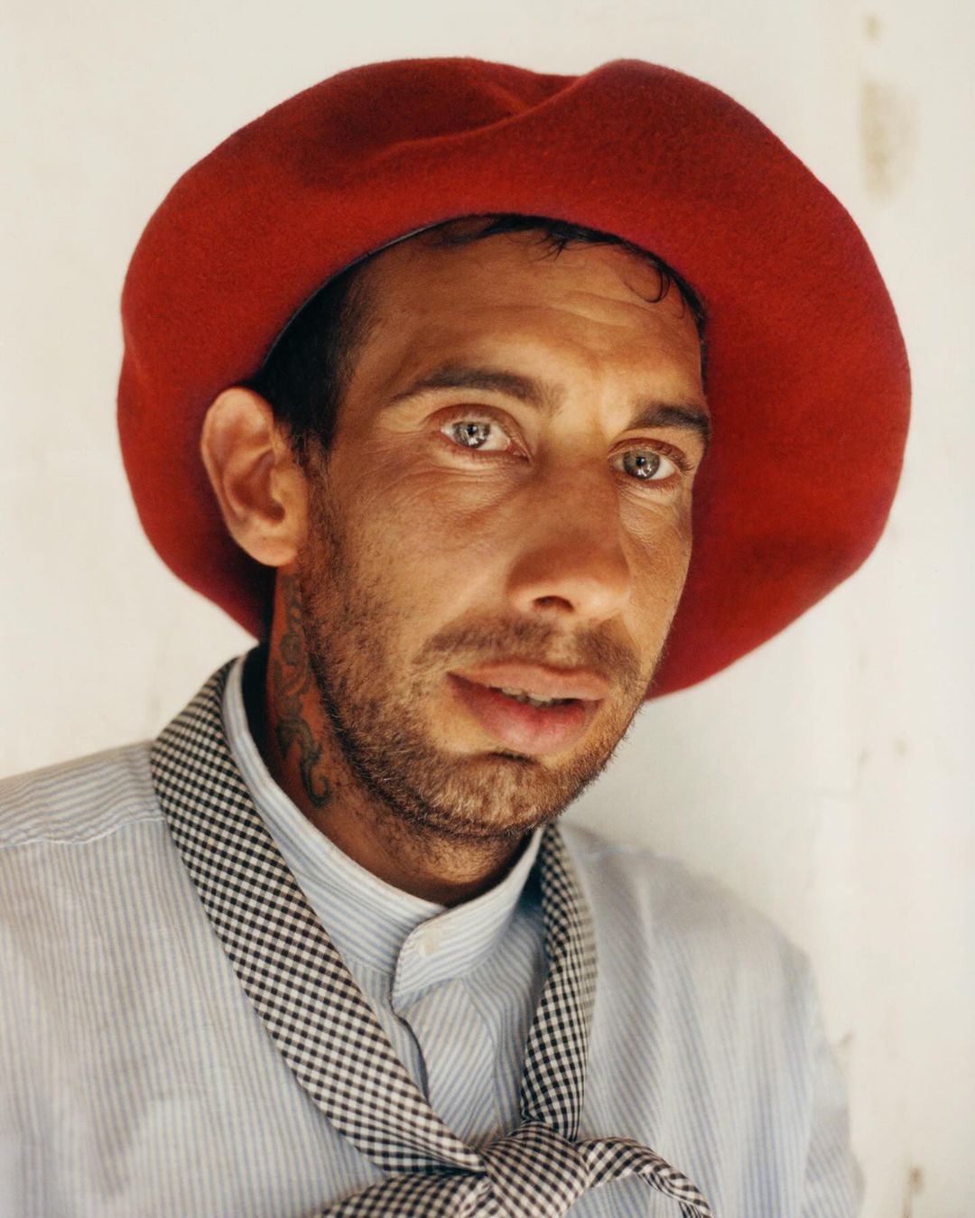 Close-up portrait of an adult male wearing a red beret and a blue and white striped shirt with a black and white checkered scarf.