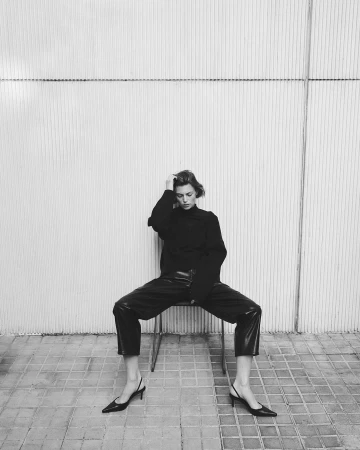 Monochrome fashion photograph of a woman seated on a chair against a textured tiled wall by Rodrigo Carmuega.