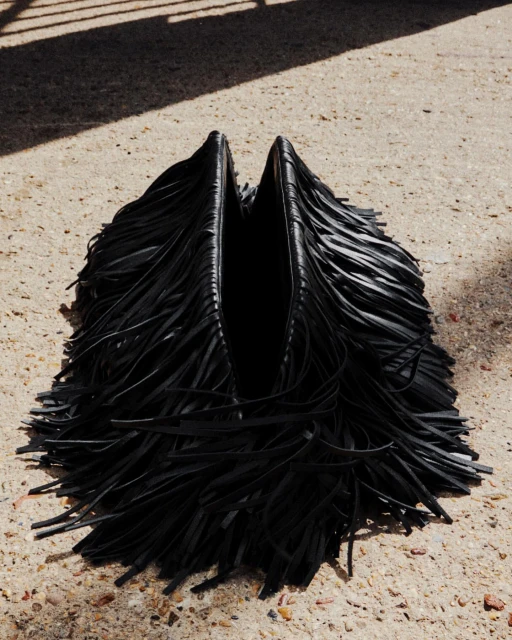 Black fringe hobo bag on concrete surface, illuminated by sunlight creating shadows. Fashionable and stylish shoulder bag.