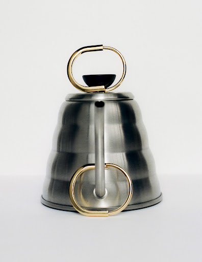 Elevated shot of a silver-colored tea kettle with gold handle, minimalist design against a white background, product photography.