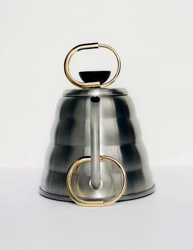Elevated shot of a silver-colored tea kettle with gold handle, minimalist design against a white background, product photography.