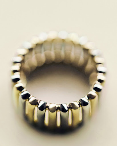Close-up macro shot of a metallic fluted ring with gold and silver segments against a soft neutral background