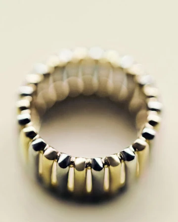 Close-up macro shot of a metallic fluted ring with gold and silver segments against a soft neutral background