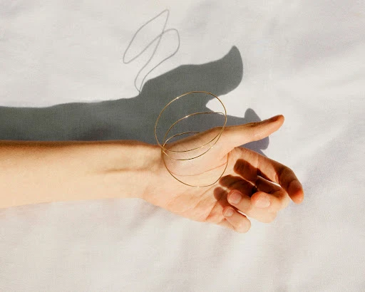 Close up of a hand wearing thin gold bangles resting against a white background with sharp shadows cast above it.