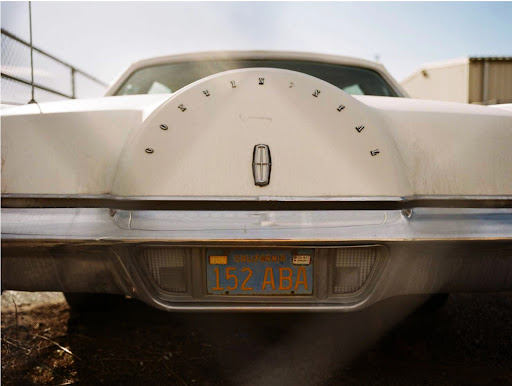 Rear view of a white vintage Lincoln Continental car with a blue and yellow California license plate in a suburban setting.