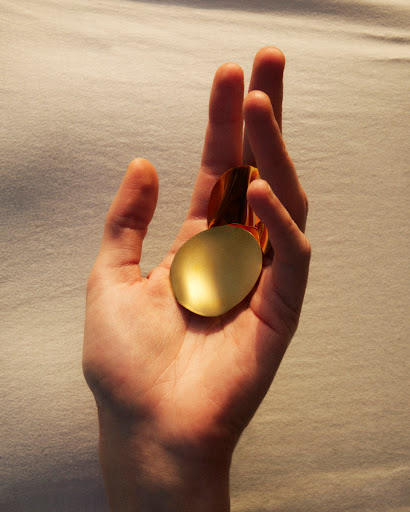 Hand holding two metallic gold geometric shapes in an eye-level indoor shot with soft lighting and a solid textured background.