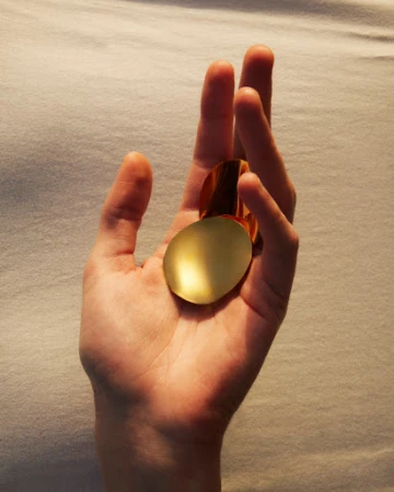 Hand holding two metallic gold geometric shapes in an eye-level indoor shot with soft lighting and a solid textured background.