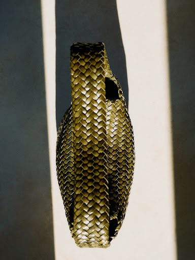 Close-up studio shot of a woven handbag in warm lighting, highlighting the textures and craftsmanship of the accessory.