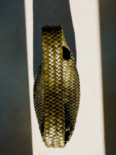 Close-up studio shot of a woven handbag in warm lighting, highlighting the textures and craftsmanship of the accessory.