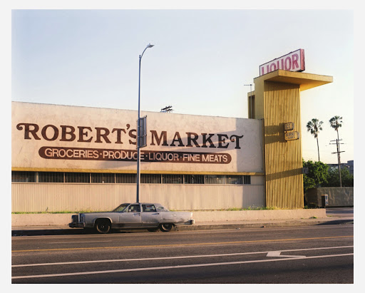 Vintage photo of a Robert's Market grocery store with a classic car parked outside, featuring a 'LIQUOR' sign in daytime.
