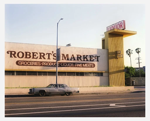Vintage photo of a Robert's Market grocery store with a classic car parked outside, featuring a 'LIQUOR' sign in daytime.