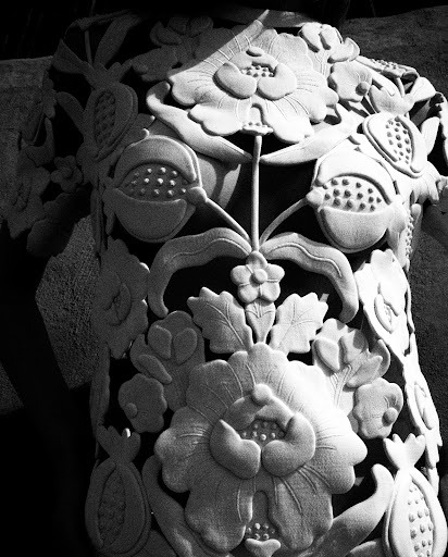 Monochrome image of an ornate architectural detail with carved floral and fruit motifs, showcasing intricate stone craftsmanship.