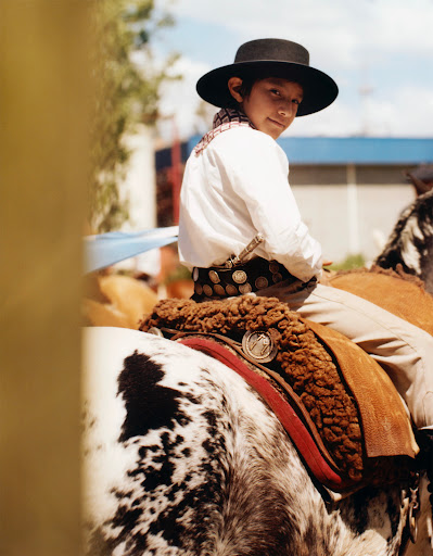 Young gaucho in traditional attire smiles on horseback in a rural outdoor setting, showcasing cultural heritage and equestrian skills.