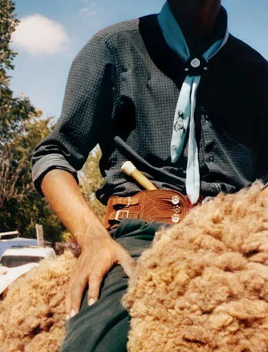 Argentinian gaucho wearing traditional shirt and neckerchief, sits atop sheepskin saddle; leather belt with knife, clear blue sky.