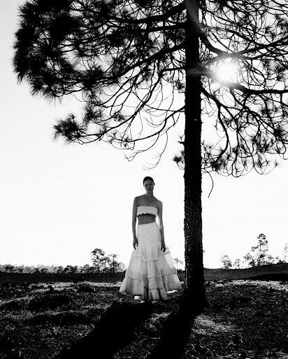 Model standing beneath a large pine tree in a monochrome landscape wearing a strapless two piece outfit