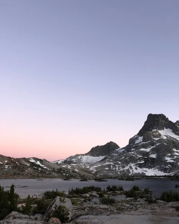 Scenic mountain range landscape view with a lake and snow on the mountain peaks against a blue, pink and purple gradient sky.