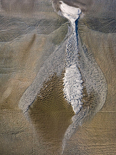 Aerial view of sand dunes and water patterns creating an abstract textured landscape formation.