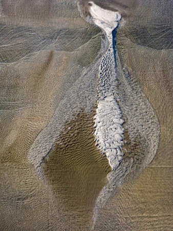 Aerial view of sand dunes and water patterns creating an abstract textured landscape formation.