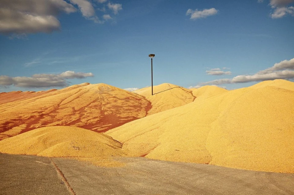 Elevated view of a large corn pile under a blue sky with white clouds and a lamppost in the center.