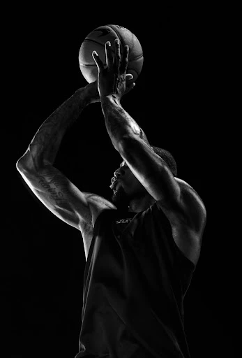 Monochrome action shot of a muscular man in a tank top about to shoot a basketball, captured in a dramatic, high-contrast profile.