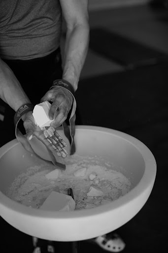 Monochrome shot of adult male gymnast chalking hands over bowl in indoor gym, preparing for fitness workout with athletic gear.