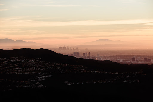Distant cityscape view of Los Angeles, California, featuring silhouetted mountains, hazy skyline, and a gradient sky at dusk.