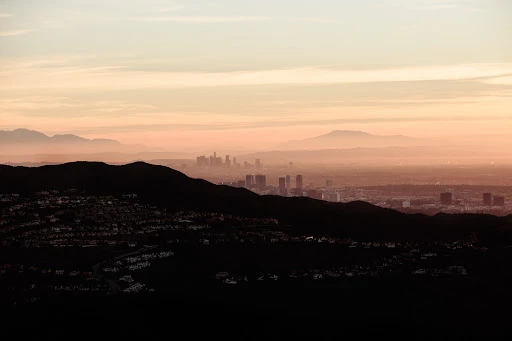 Distant cityscape view of Los Angeles, California, featuring silhouetted mountains, hazy skyline, and a gradient sky at dusk.