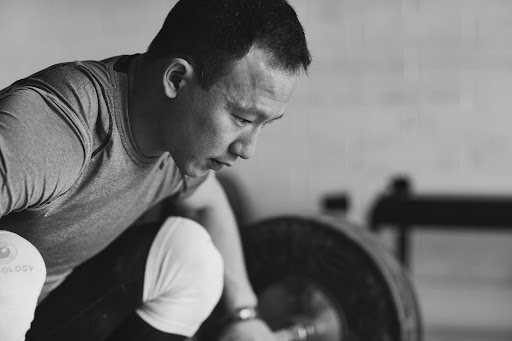 Monochrome shot of an adult male weightlifter preparing to lift a barbell in a gym with a focus on strength training.