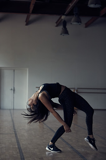 Athletic woman in black activewear bends over backwards in a studio, showcasing her flexibility and fitness in a dynamic pose.