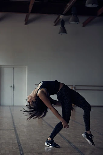 Athletic woman in black activewear bends over backwards in a studio, showcasing her flexibility and fitness in a dynamic pose.