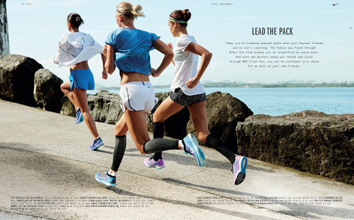 Three women runners in athletic wear stride along a paved path next to a sea. They are captured in motion with natural daylight.