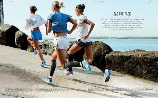 Three women runners in athletic wear stride along a paved path next to a sea. They are captured in motion with natural daylight.
