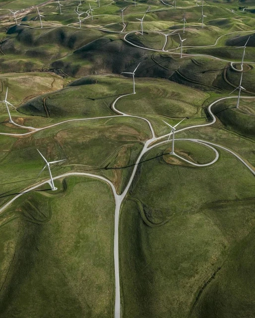 Aerial view of wind turbines on rolling green hills with white gravel paths winding through the landscape, generating clean energy.