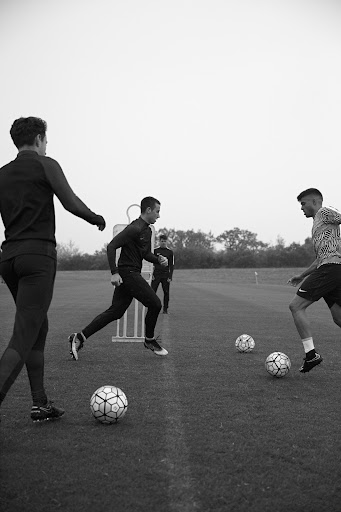 Monochrome shot of soccer players practicing drills on a grassy field, with soccer balls and training equipment visible.