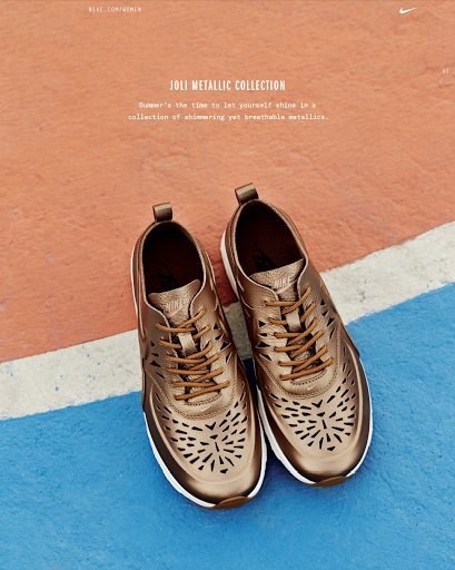 Studio shot of bronze-toned Nike athletic shoes with a cut-out pattern on a textured surface with a blue and peach background.