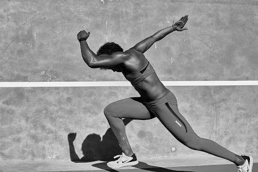 Black and white photograph of an athlete in motion, wearing sportswear against a textured wall, showcasing strength and determination.
