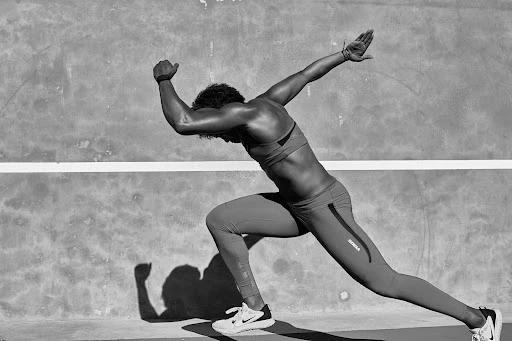 Black and white photograph of an athlete in motion, wearing sportswear against a textured wall, showcasing strength and determination.
