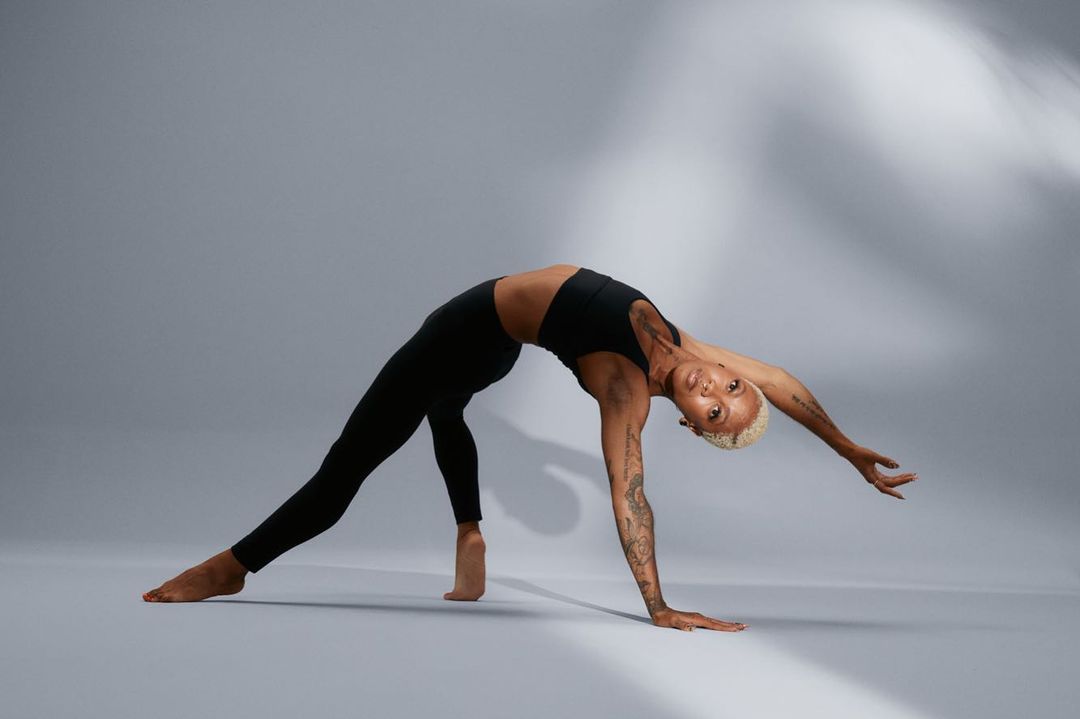 An adult woman with blonde hair is in a backbend yoga pose wearing a black sports bra and black leggings in a studio setting.