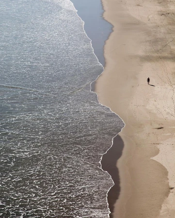 Aerial view of a lone person walking along a sandy beach beside ocean waves breaking on the shore