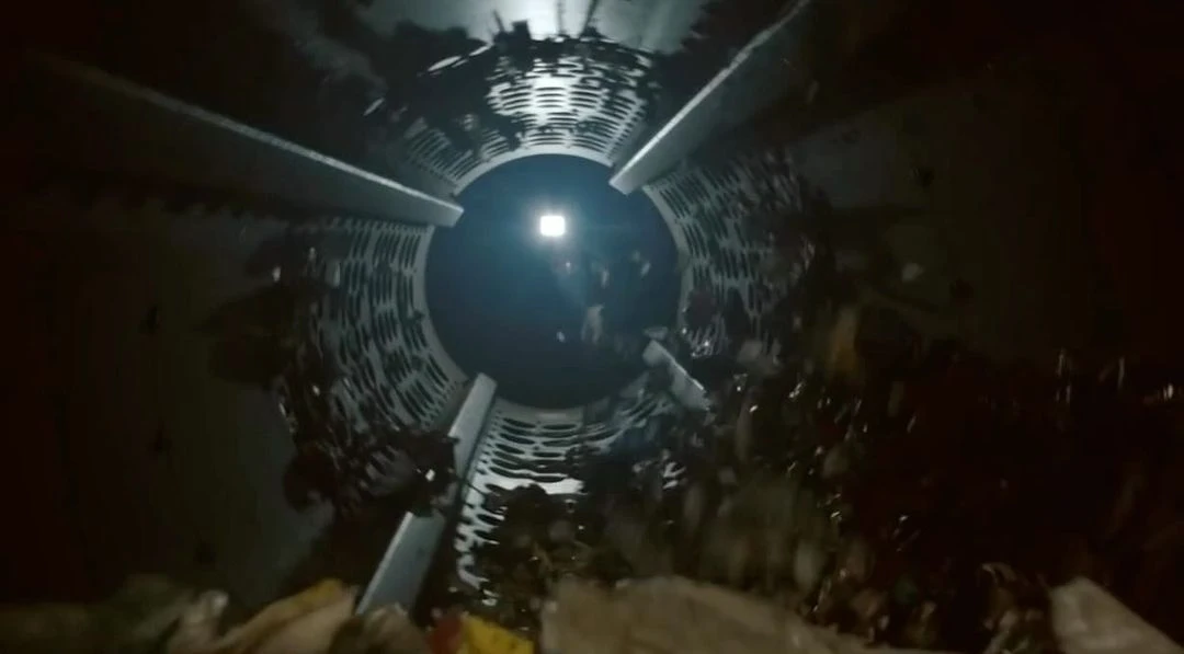 Inside a dark metal cylinder with internal structural ribs, illuminated by a bright light at the far end, some debris visible.
