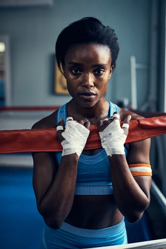 Portrait of a strong, determined African American woman in athletic wear, standing in a boxing ring with bandaged hands.