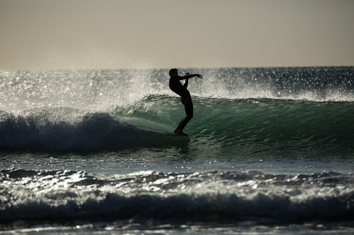 Silhouette of a surfer riding a wave in the ocean under a bright sky with glistening water and whitecaps in the foreground.