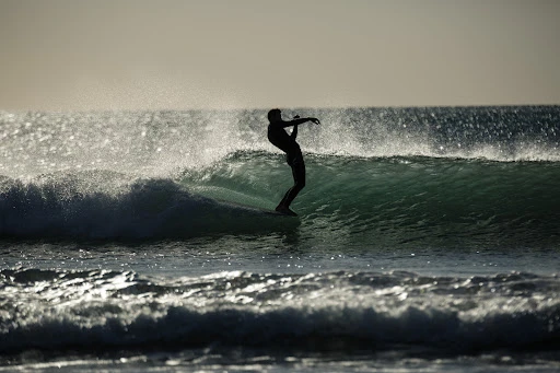 Silhouette of a surfer riding a wave in the ocean under a bright sky with glistening water and whitecaps in the foreground.