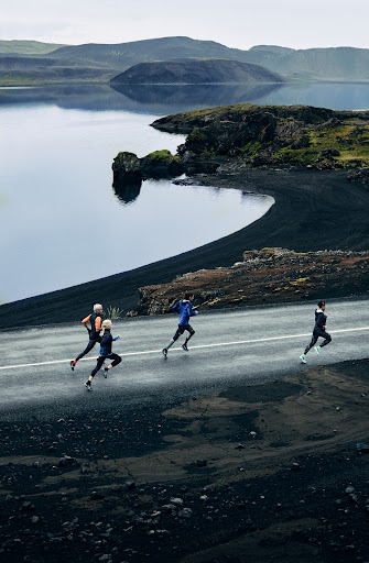 Group of runners on a road next to a lake and volcanic landscape. Overcast day, athletic wear, running shoes, and natural scenery.