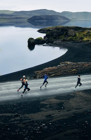 Group of runners on a road next to a lake and volcanic landscape. Overcast day, athletic wear, running shoes, and natural scenery.