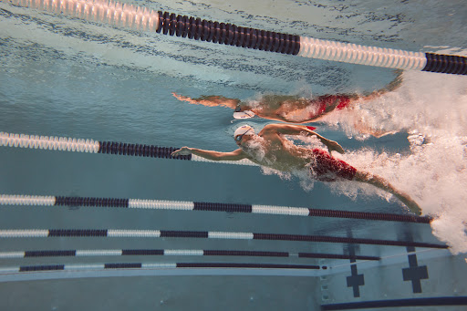 Underwater shot of two adult male swimmers in red trunks racing in a pool with lane markers, showcasing athleticism and aquatic sport.