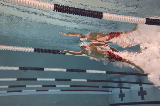 Underwater shot of two adult male swimmers in red trunks racing in a pool with lane markers, showcasing athleticism and aquatic sport.