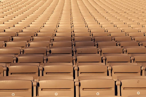 Rows of empty tan-colored stadium seats stretch into the distance, creating a symmetrical and repetitive pattern under even lighting.